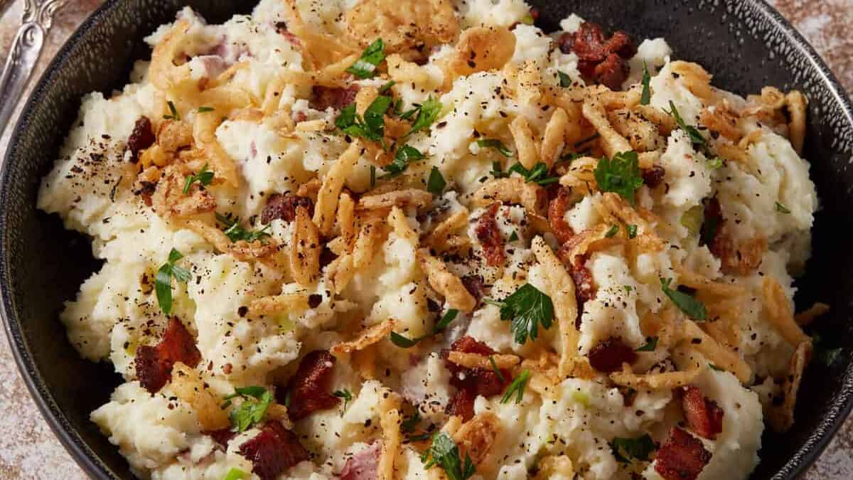 A bowl of loaded mashed potatoes with a small bowl of crispy onions.