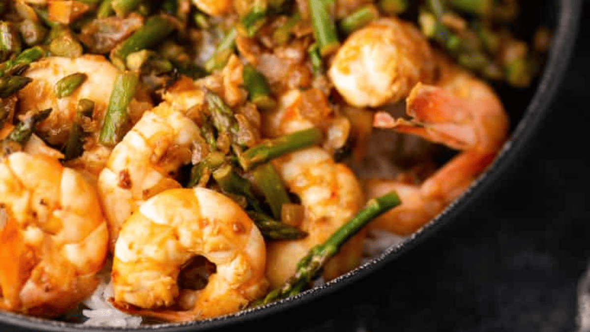 Close-up of a dish featuring cooked shrimp, chopped asparagus, and a savory sauce served over white rice in a black bowl—a delicious example of flavorful Asian dishes.
