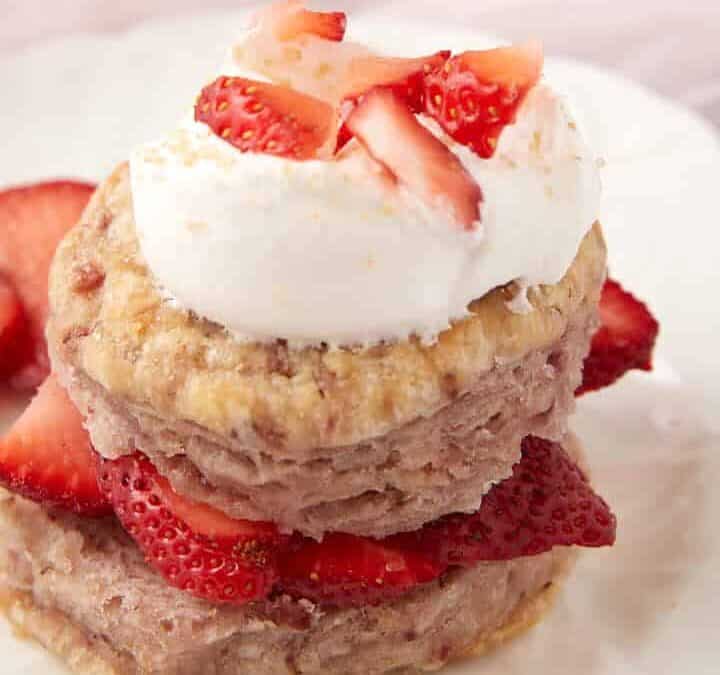A strawberry biscuit with fresh strawberries and whipped cream.