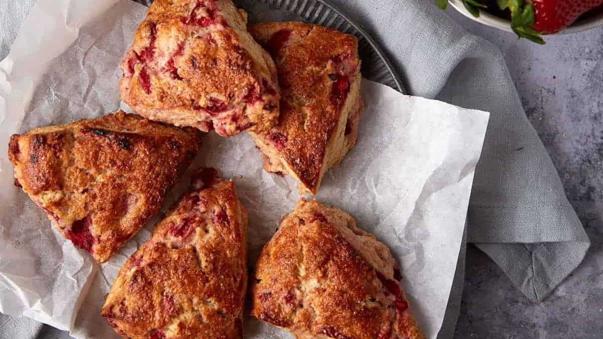Strawberry scones on parchment paper next to a bowl of strawberries.