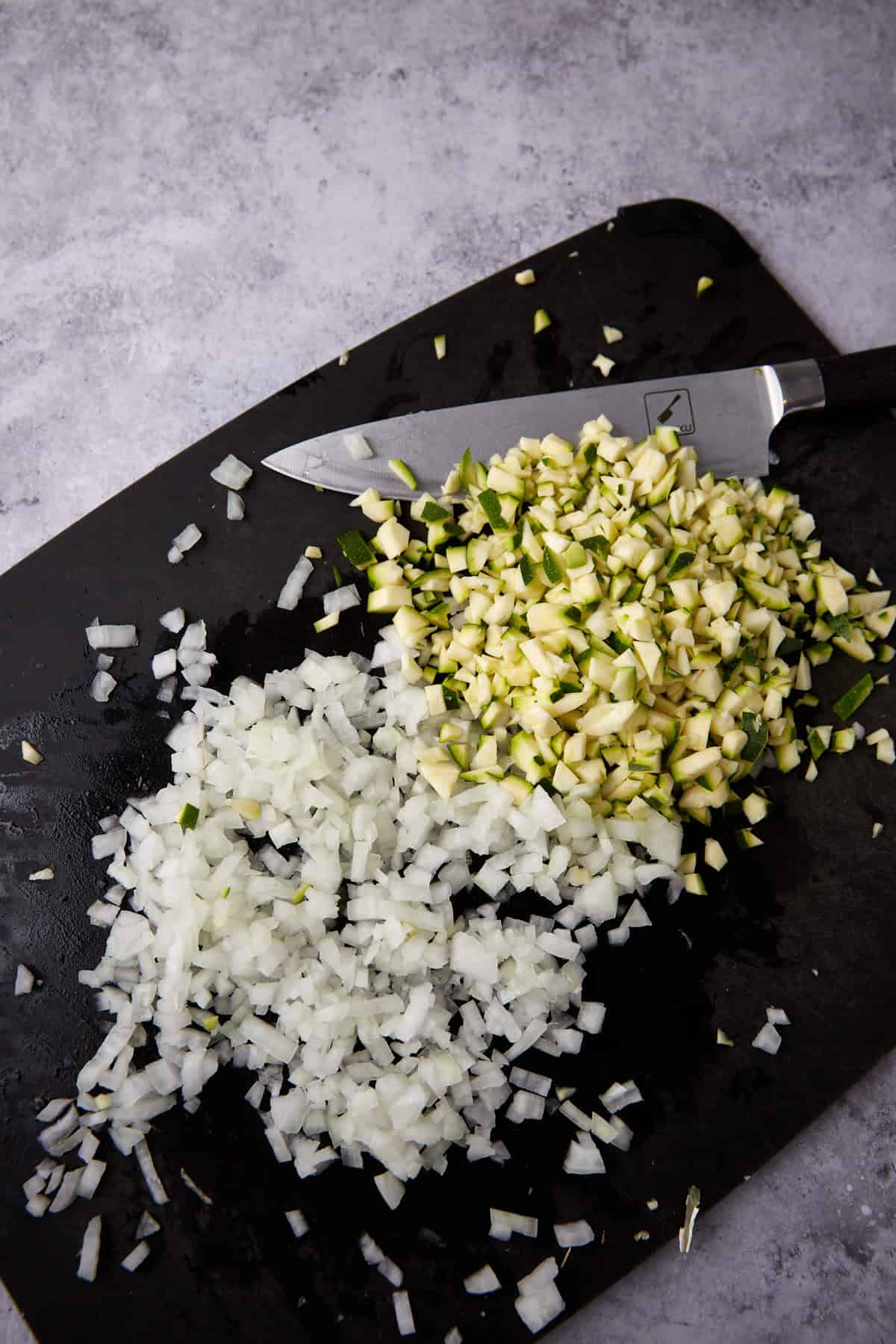 chopped zucchini and onion on a cutting board with a knife.
