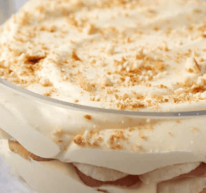 A glass bowl filled with layers of creamy dessert, likely banana pudding, showcases the irresistible appeal of layered desserts, topped with crumbled cookies or wafers.