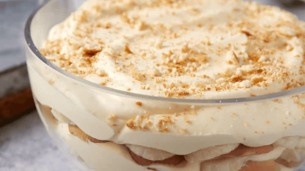 A glass bowl filled with layers of creamy dessert, likely banana pudding, showcases the irresistible appeal of layered desserts, topped with crumbled cookies or wafers.