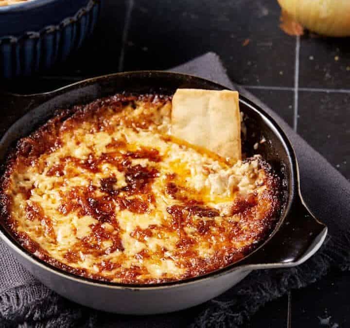 A pita chip in a bowl of onion dip.
