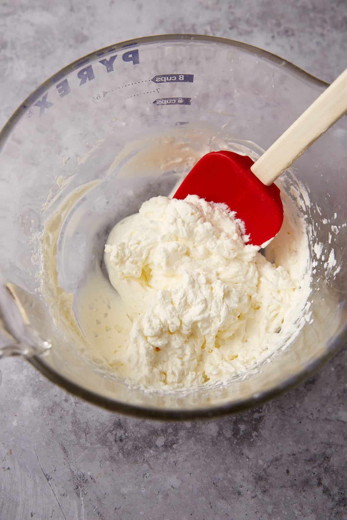 whipped cream mixture in a glass mixing bowl with a spatula.