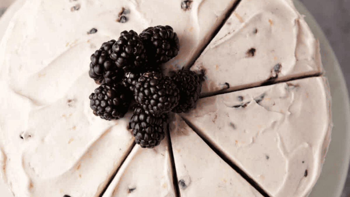 A close-up of a round, sliced cake with creamy white frosting, topped with a cluster of fresh blackberries in the center—an elegant nod to viral vintage recipes.