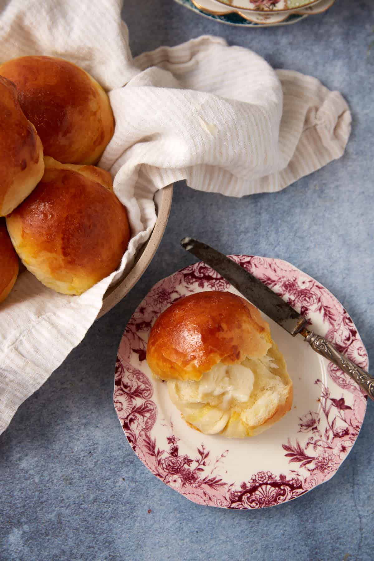 buttermilk yeast roll cut in half with butter on a plate with a knife on the side and the rest of the rolls on the other side.