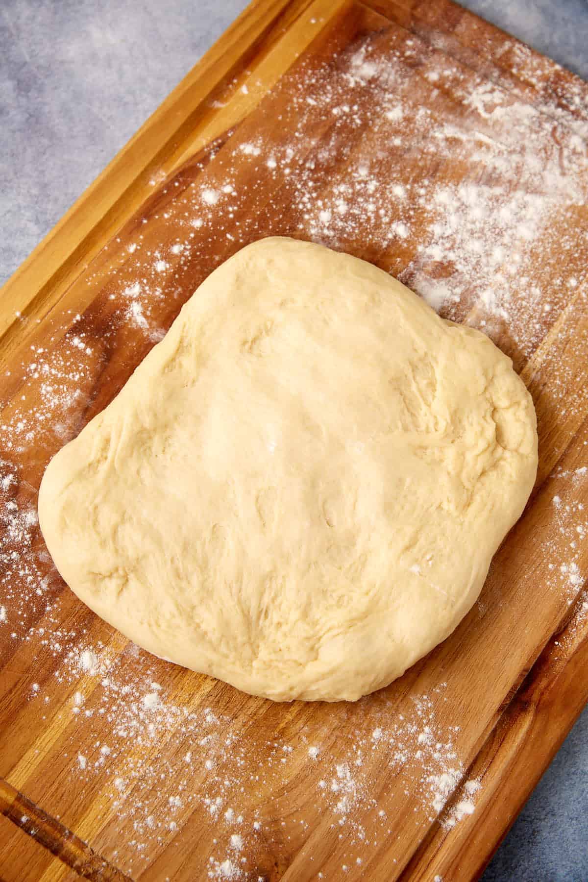 buttermilk yeast roll dough rolled out on a wooden cutting board.