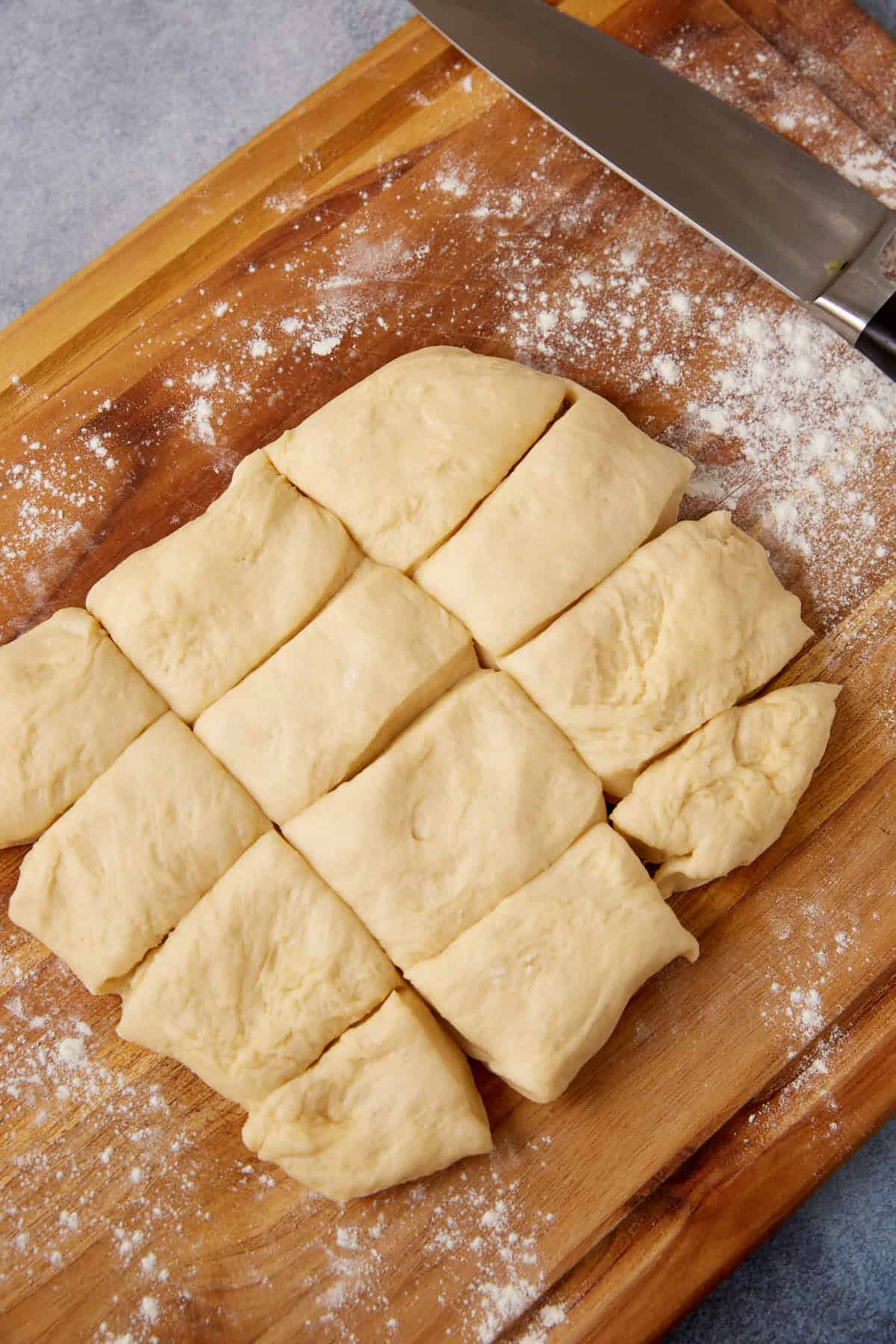 buttermilk yeast roll dough rolled out and cut into rectangles on a wooden cutting board.