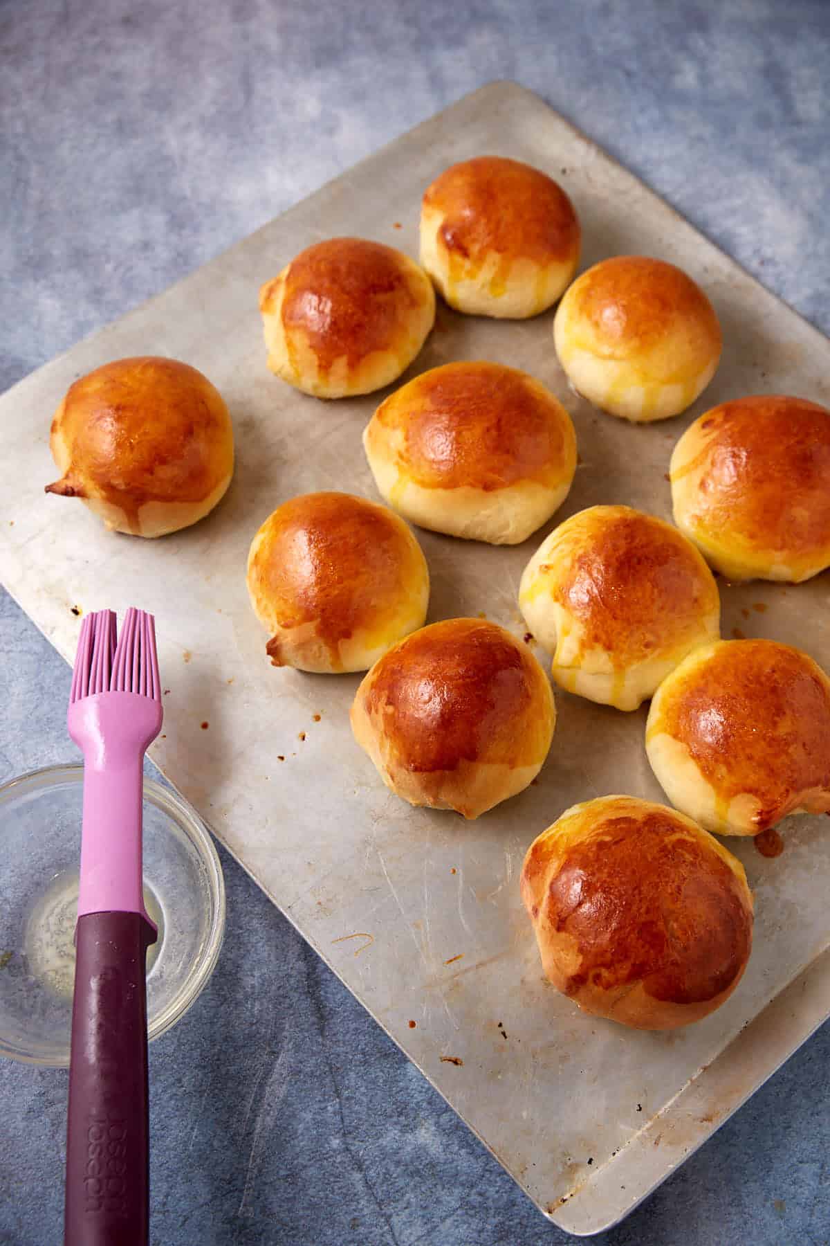 buttermilk yeast rolls on a baking sheet with the melted butter and a pastry brush on the side.