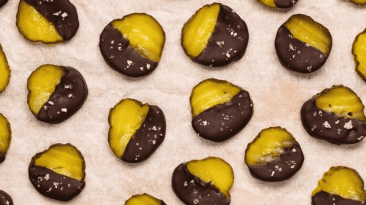 Rows of yellow dried mango slices, half-dipped in dark chocolate and sprinkled with flaky sea salt, are arranged on parchment paper—perfect for adding a sweet and salty twist to your dessert dishes.