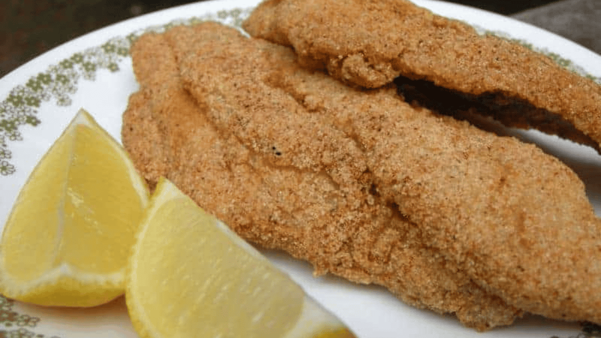 Two pieces of golden-brown fried fish fillets on a white plate with a green floral border, served with two wedges of fresh lemon—a classic favorite from before air fryers changed the way we cook.