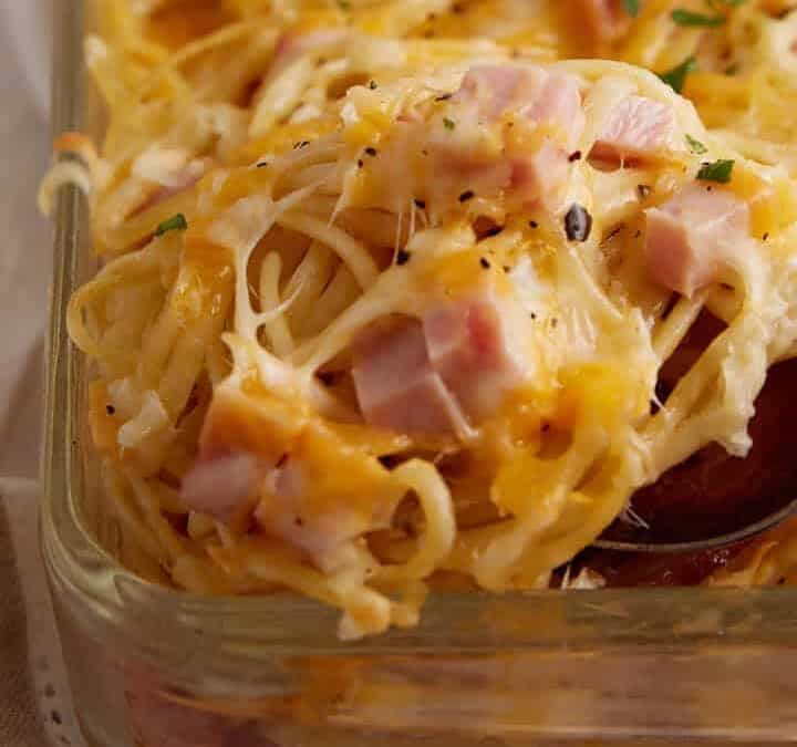 A spoon scooping out a serving of ham and cheese casserole.