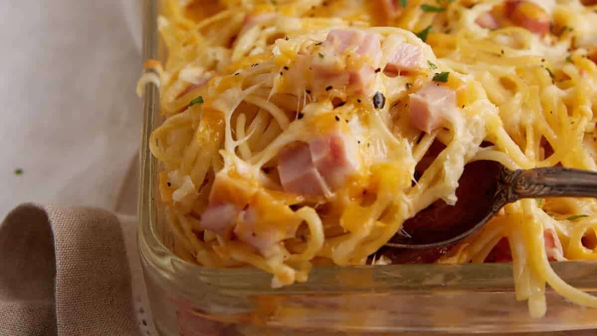 A spoon scooping out a serving of ham and cheese casserole.