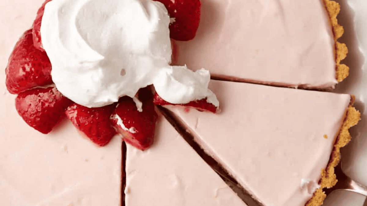 A strawberry cream pie with a graham cracker crust, topped with sliced strawberries and a dollop of whipped cream. One slice has been cut and slightly separated from the pie—one of those old fashioned pie favorites everyone loves.