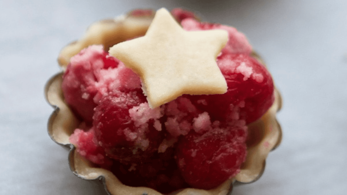 A small tart inspired by viral vintage recipes, filled with red berries and pink sugar crystals, topped with a star-shaped piece of pastry.