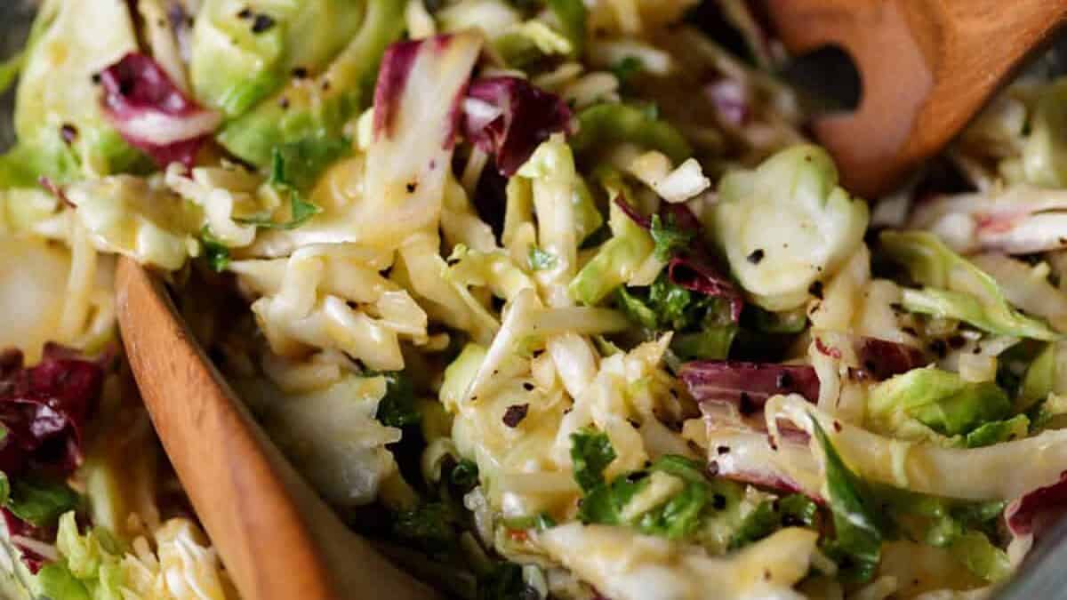 A bowl of peach coleslaw without mayo in a bowl with wooden spoons.