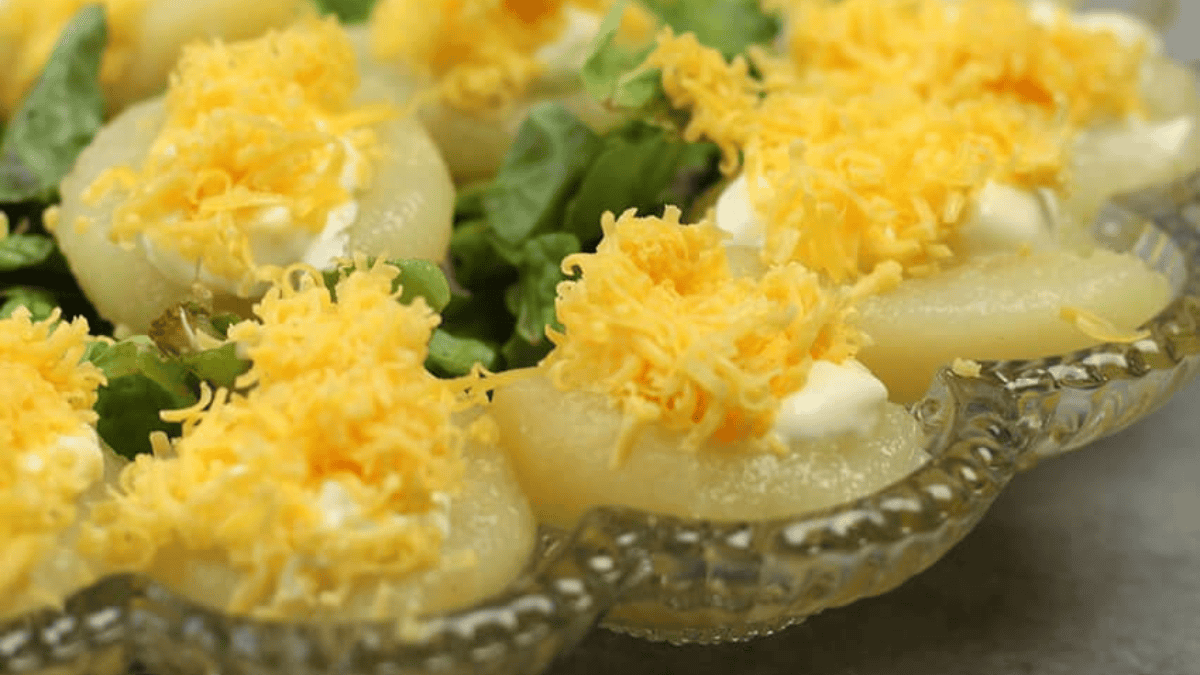 Glass platter with pear halves topped with dollops of mayonnaise and shredded cheddar cheese, garnished with lettuce leaves underneath—an unexpected yet classic addition to your Easter dishes.