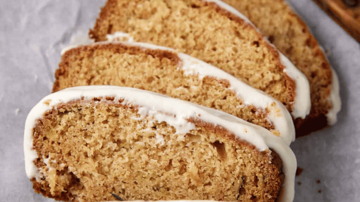 Four slices of moist brown banana bread with white icing on top, arranged on parchment paper—perfect for a spring brunch treat.