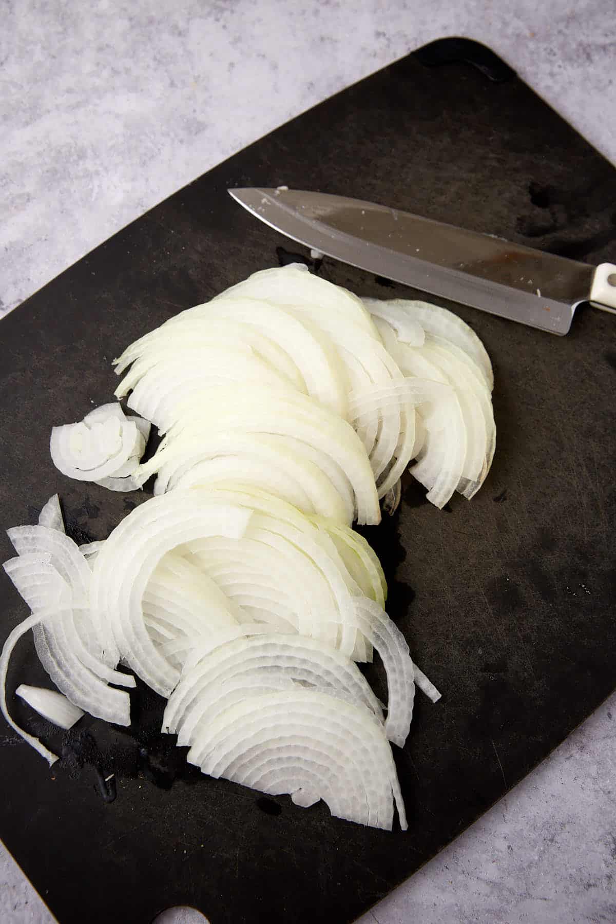 sliced onions on a cutting board with a knife.