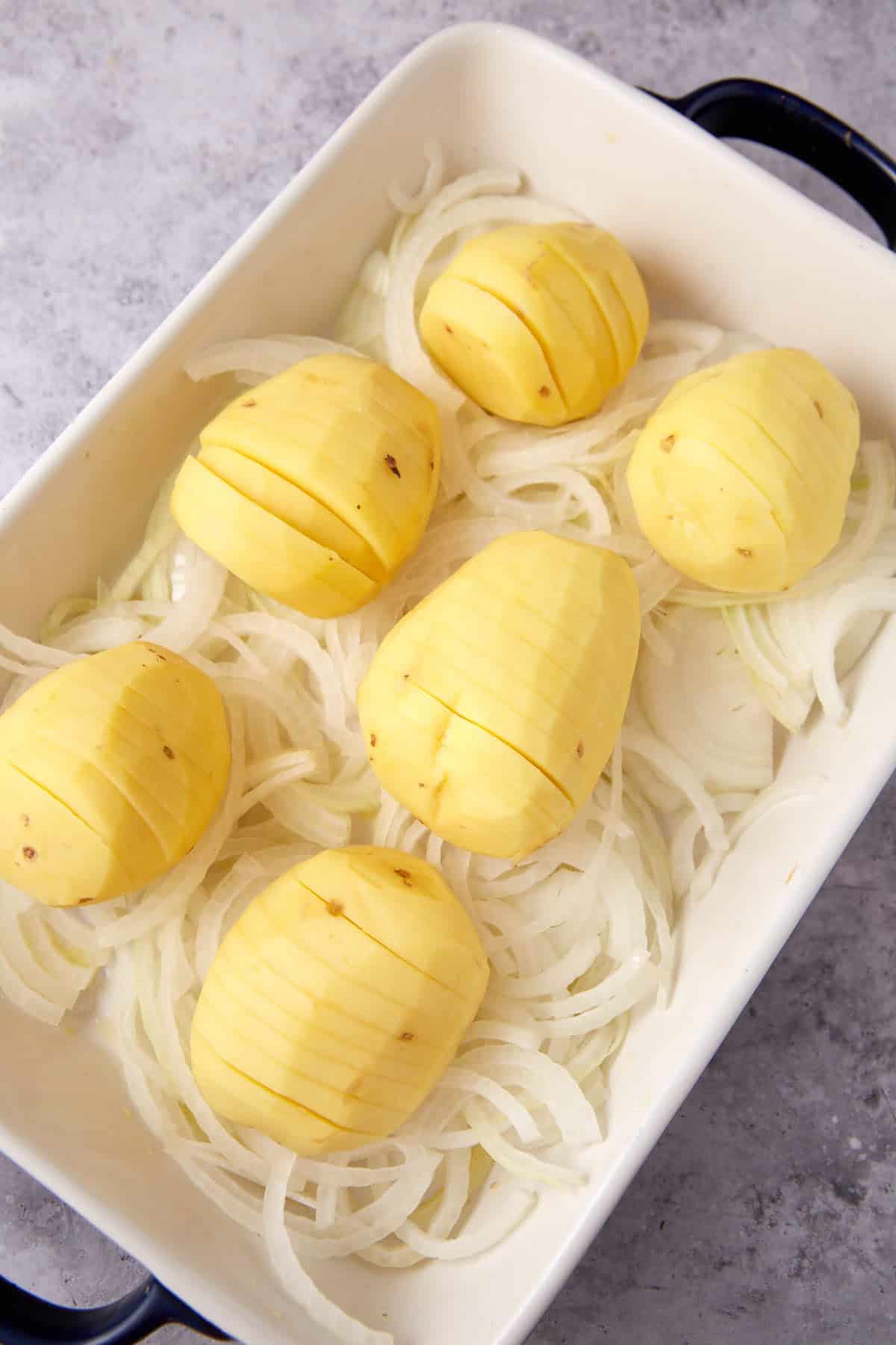 hasselback Yukon gold potatoes on top of sliced onions in baking dish.