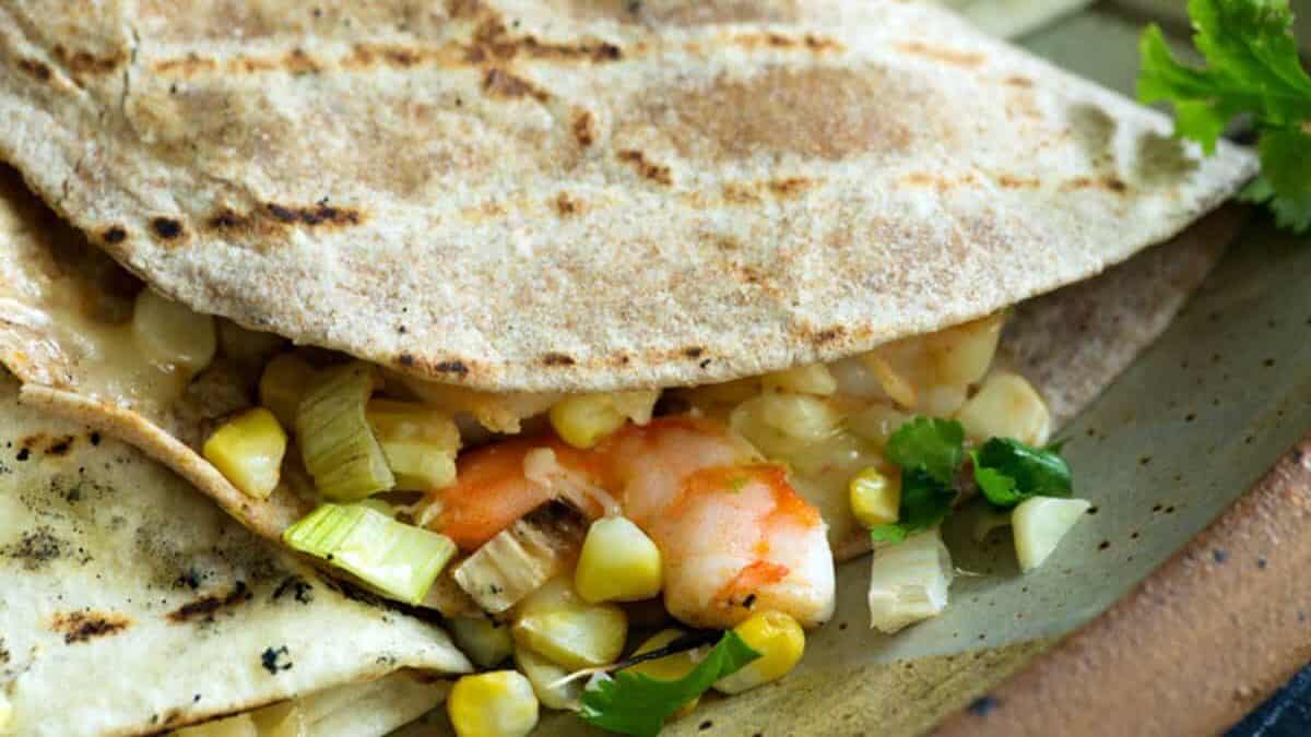A close-up of a grilled quesadilla filled with shrimp, corn, melted cheese, green onions, and fresh cilantro on a plate—perfect for adding to your Cinco de Mayo recipes.