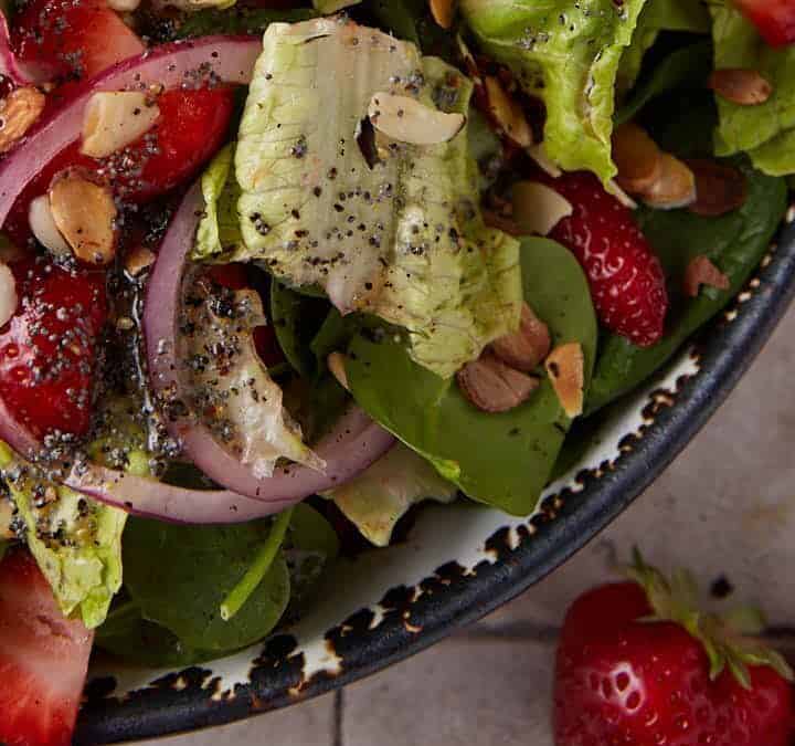 A bowl of spinach and strawberry salad covered with a poppy seed dressing.