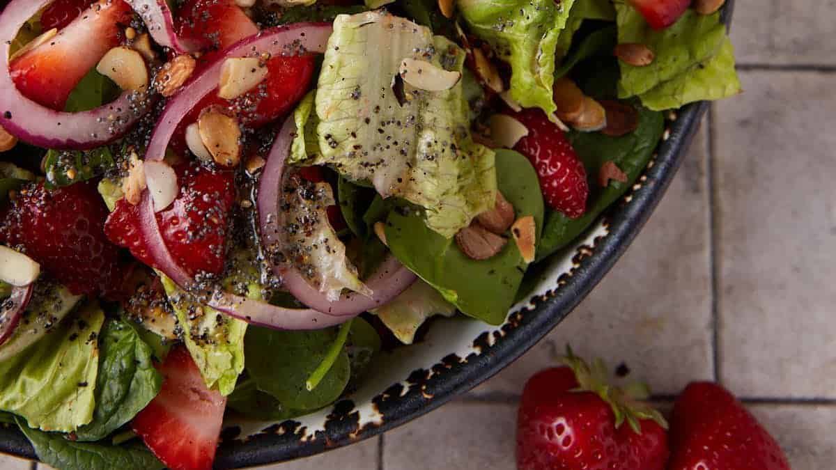 A bowl of spinach and strawberry salad covered with a poppy seed dressing.
