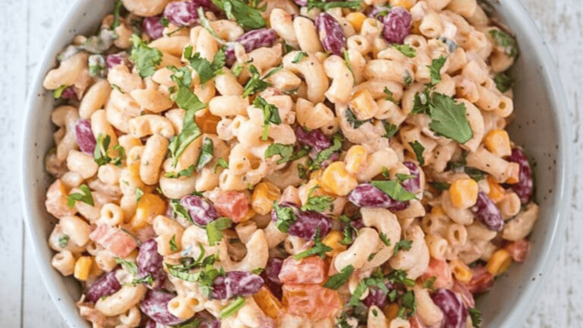 A bowl of creamy macaroni salad with kidney beans, corn, diced tomatoes, green peas, and fresh cilantro garnish—just like one of grandma’s favorite spring dishes.