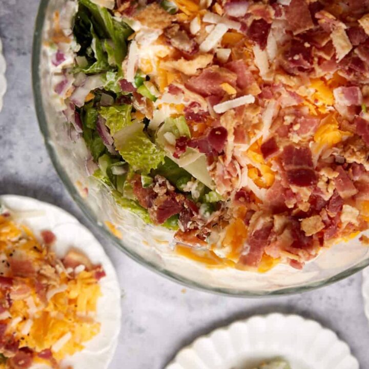 A bowl of seven layer salad next to individual servings.