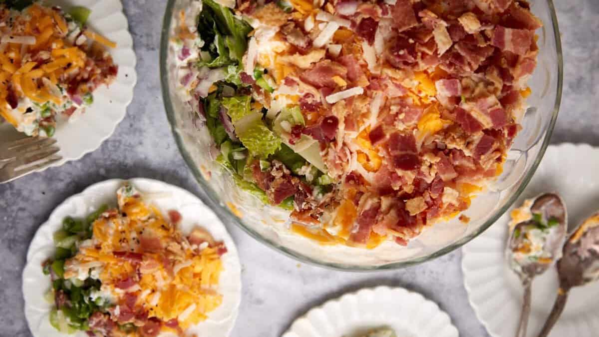 A bowl of seven layer salad next to individual servings.
