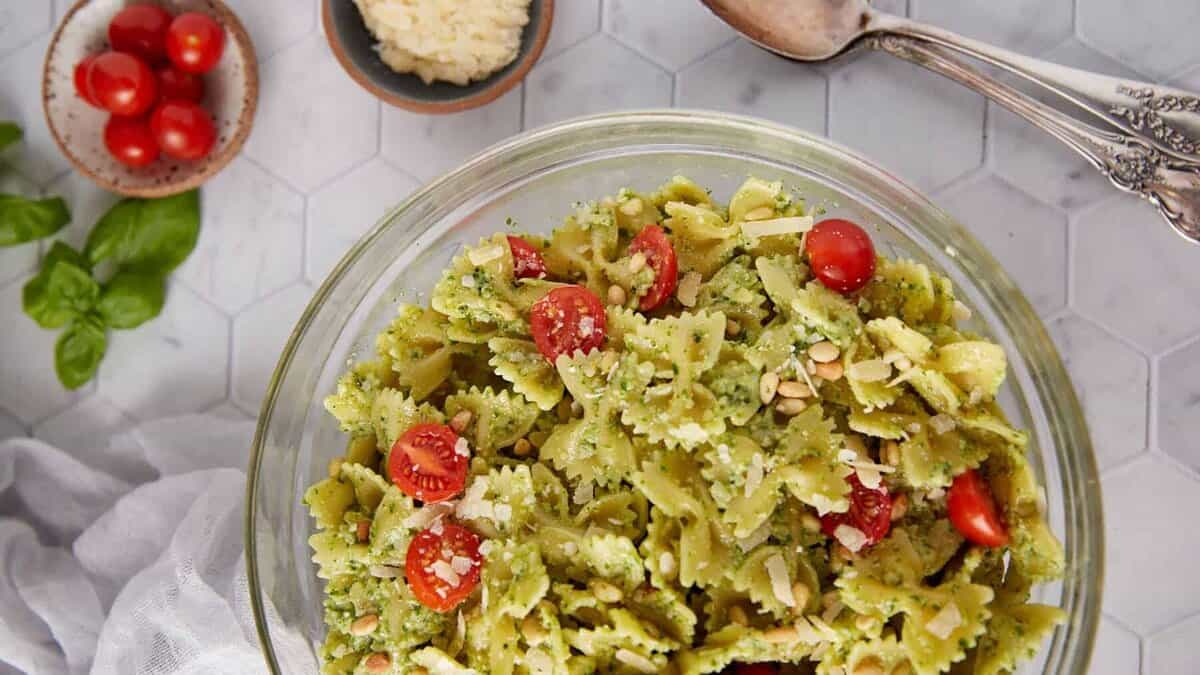 Delicious pesto pasta salad with fresh basil and cherry tomatoes in a glass bowl.