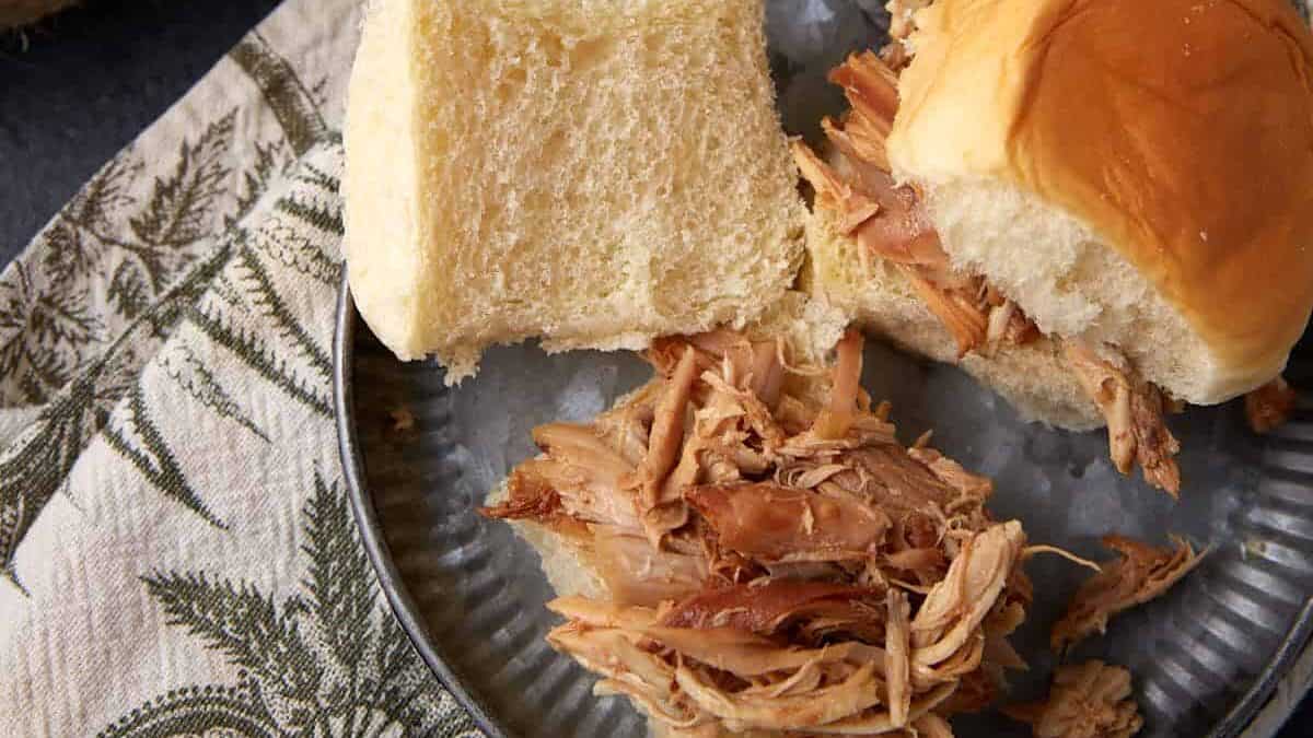 A pulled chicken slider being assembled on a plate.
