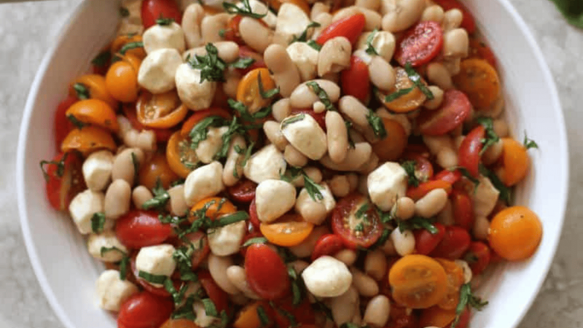 A bowl filled with a colorful salad of cherry tomatoes, white beans, mozzarella balls, and fresh basil, all mixed together.