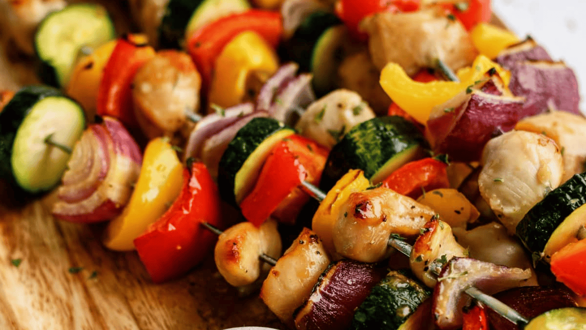Colorful chicken and vegetable skewers with zucchini, red onion, bell peppers, and grilled chicken pieces arranged on wooden skewers, served on a wooden board.