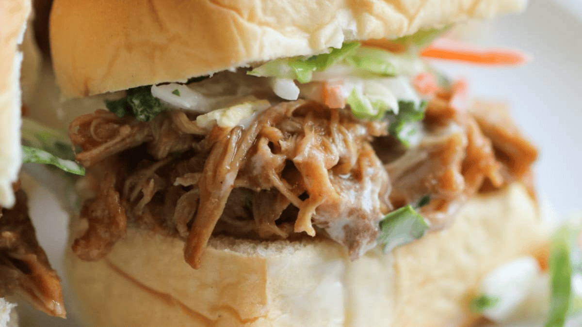 A close-up of a pulled pork sandwich on a soft bun, topped with creamy coleslaw.