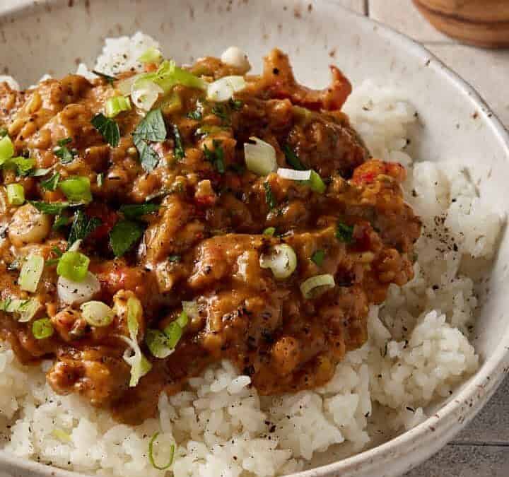 A bowl of crawfish etouffee over rice next to a napkin..