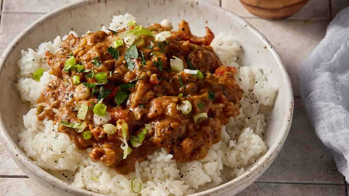 A bowl of crawfish etouffee over rice next to a napkin..