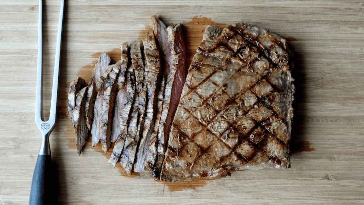 A piece of meat on a cutting board with a knife.