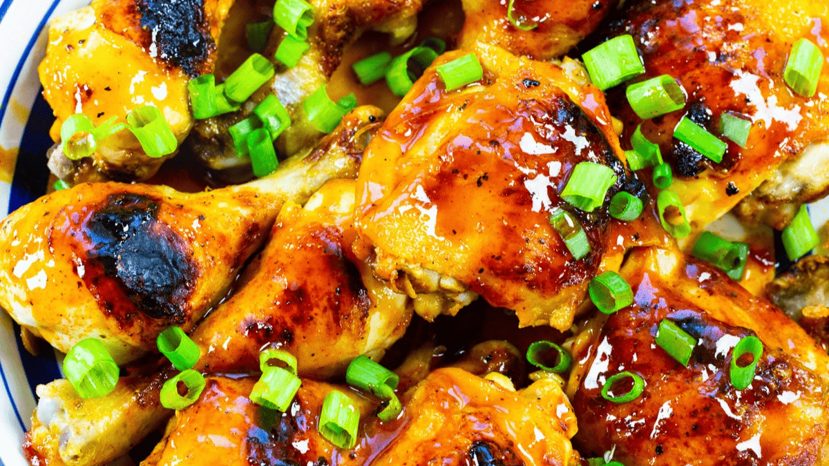A close-up of glazed baked chicken pieces topped with sliced green onions, showing a shiny, caramelized surface and vibrant colors.