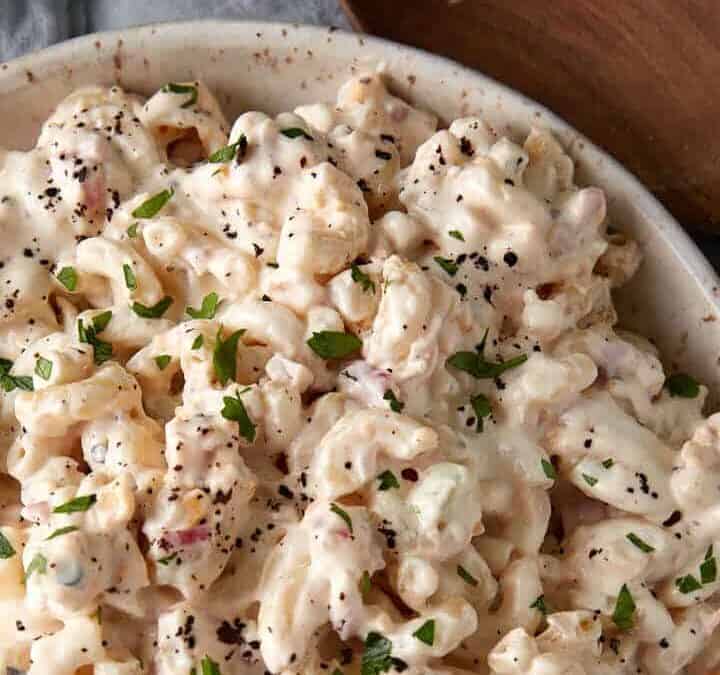 A bowl of macaroni salad next to a wooden spoon.