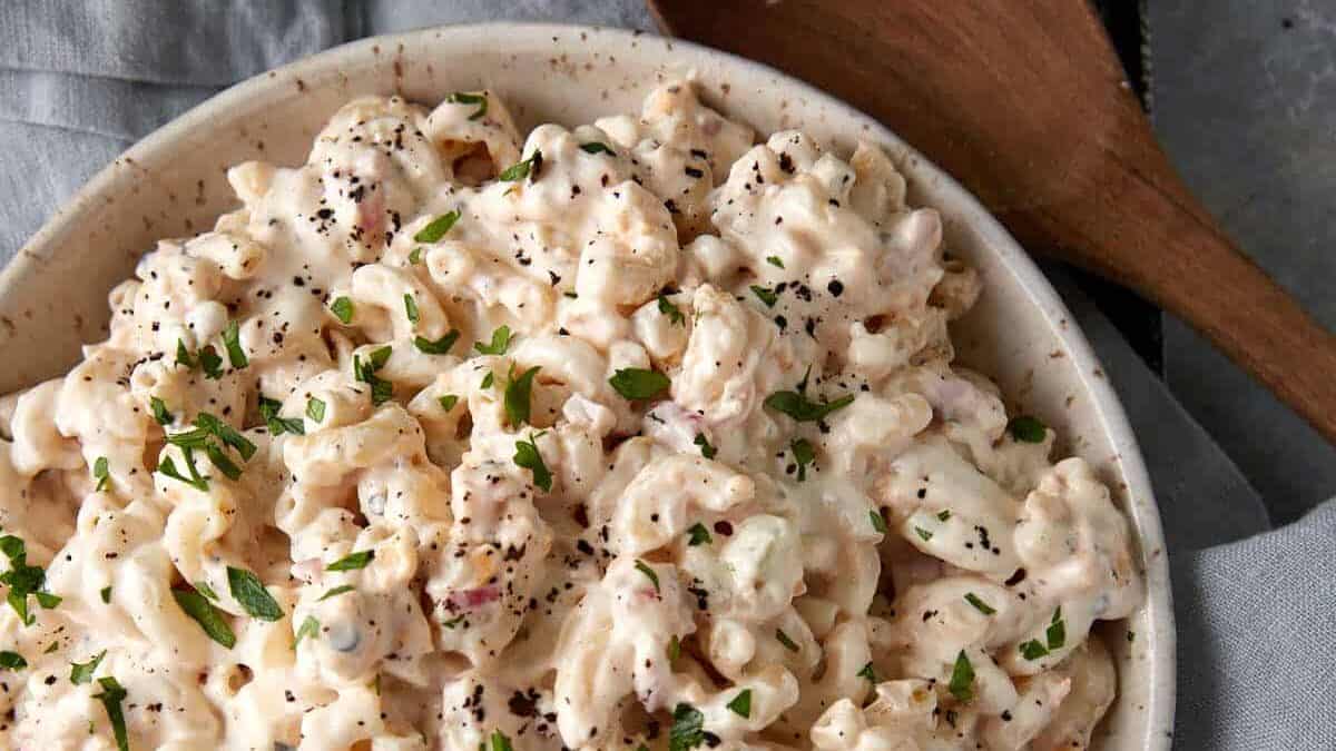 A bowl of macaroni salad next to a wooden spoon.