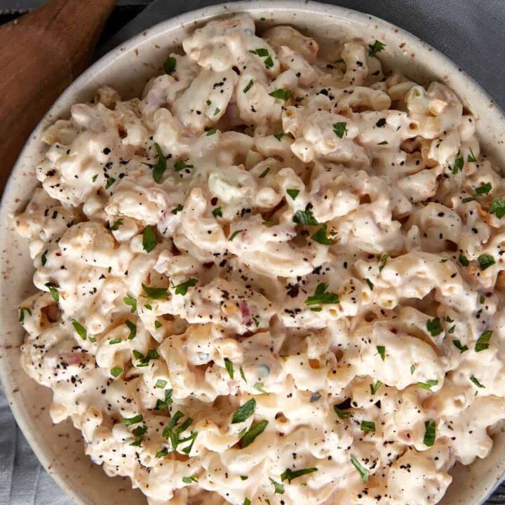 A bowl of macaroni salad next to a wooden spoon.