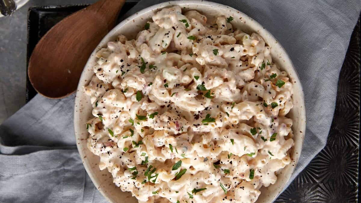 A bowl of macaroni salad next to a wooden spoon.