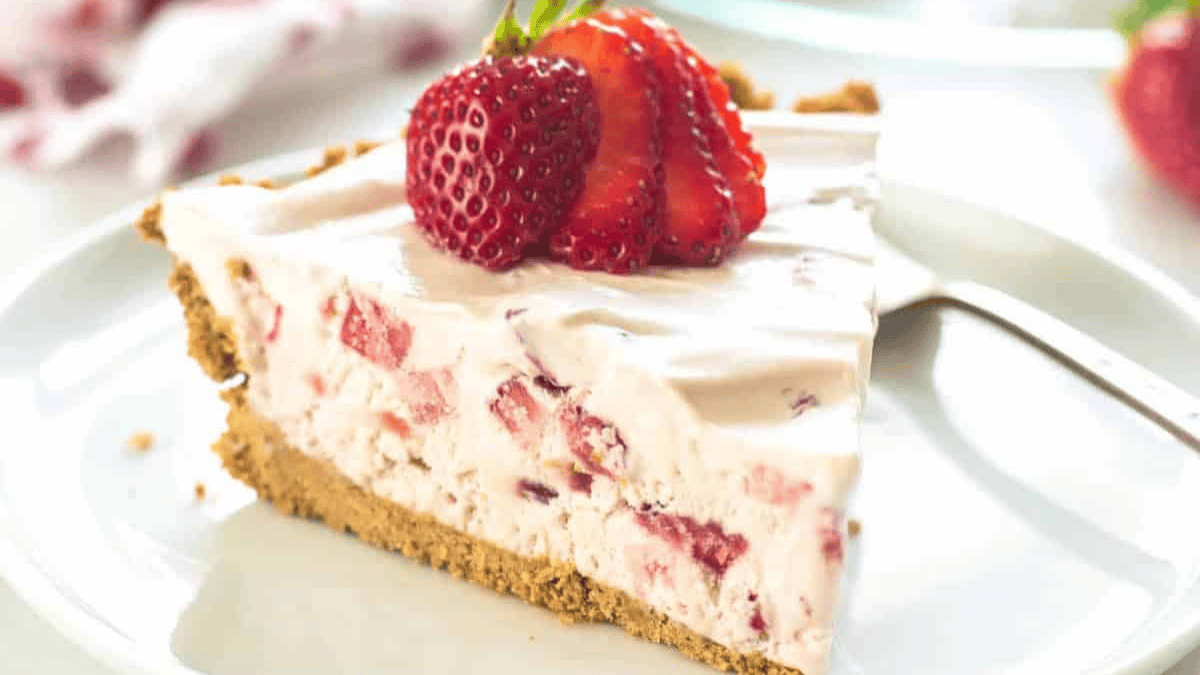 A slice of creamy strawberry cheesecake with a crumbly graham cracker crust, topped with fresh sliced strawberries, served on a white plate with a fork.