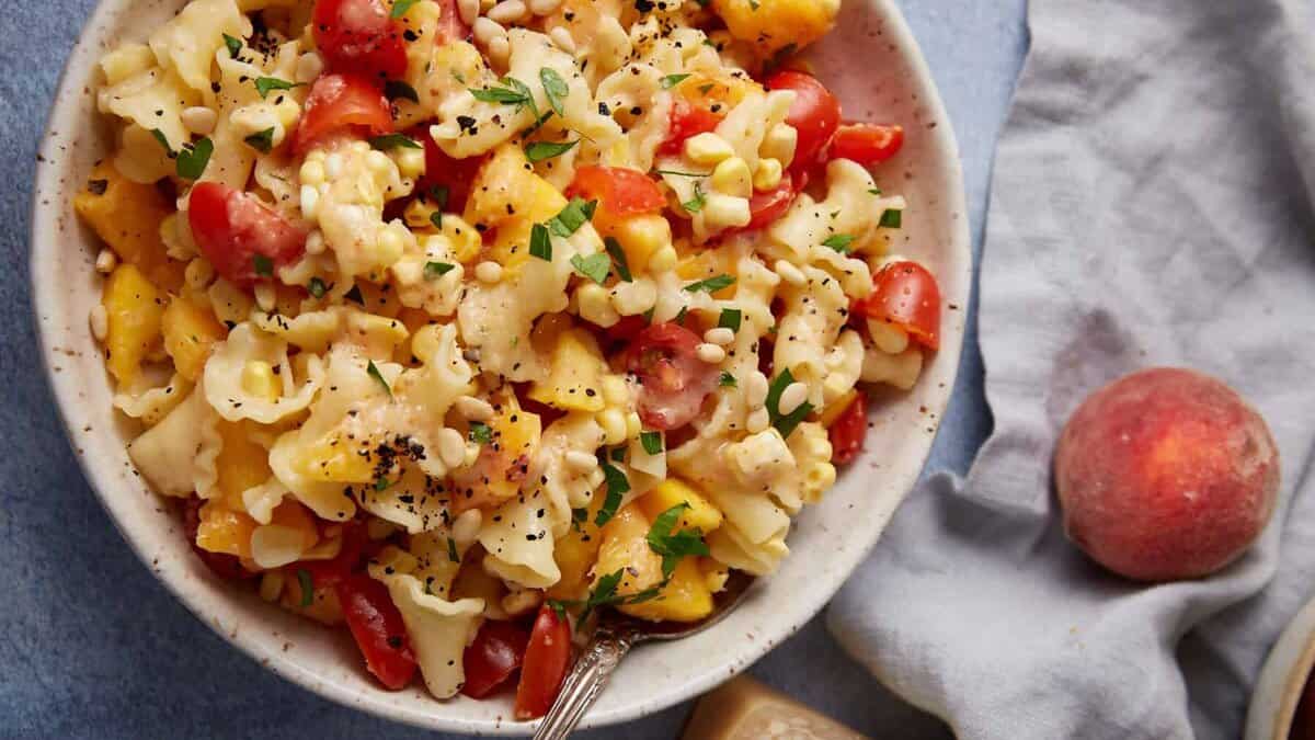 A pasta salad with peaches, corn and tomatoes in a serving bowl.