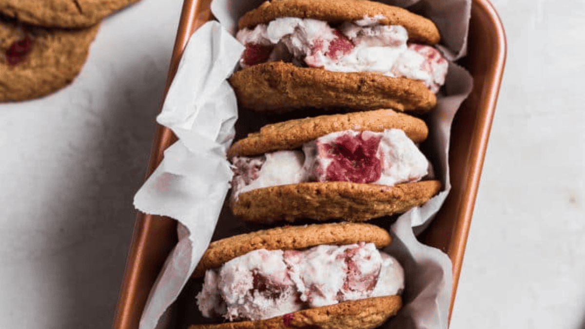 Three ice cream sandwiches made with cookies and strawberry ice cream are stacked in a parchment-lined loaf pan, perfect for celebrating rhubarb season.