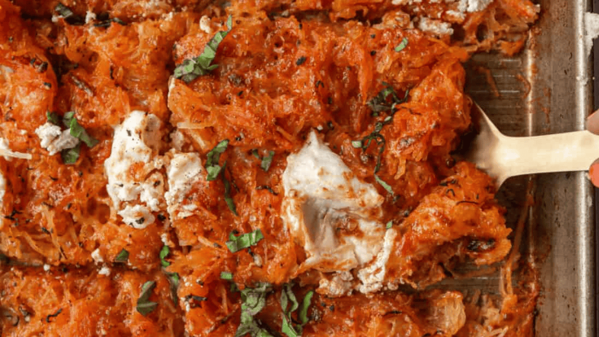 A close-up of a baked spaghetti squash casserole topped with tomato sauce, melted cheese, and fresh basil, with a serving being scooped out on a spatula.