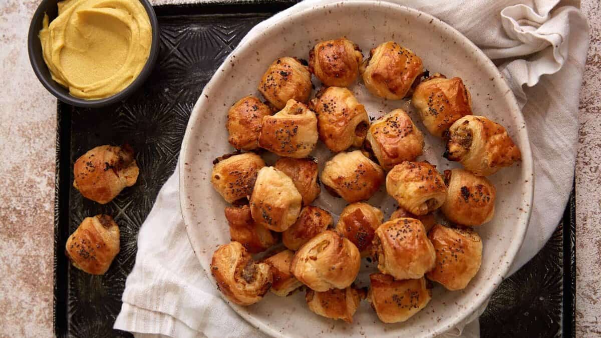 Puff pastry with apples and sausage in a bowl next to some mustard dip.