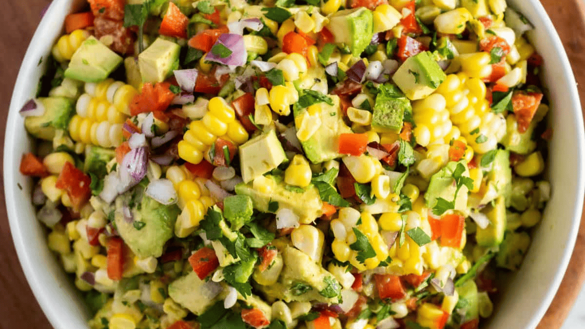 A bowl of colorful corn salad with diced avocado, red onion, red bell pepper, cilantro, and fresh corn kernels.